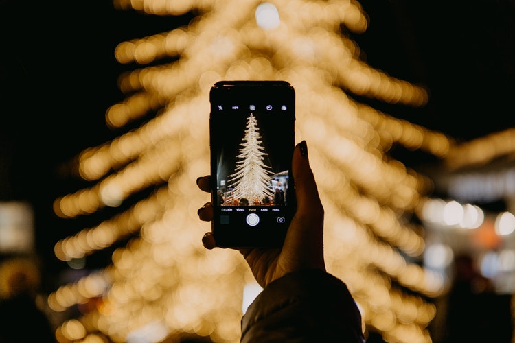 A person taking a photo of a lit Christmas tree on their phone at one of Raleigh's holiday events.